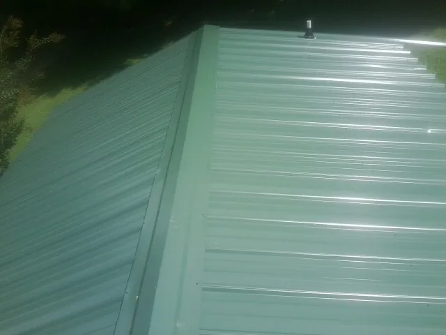 New green metal panels meeting at the ridge of a roof — Flat Roof Repair work by our crew in Kennesaw