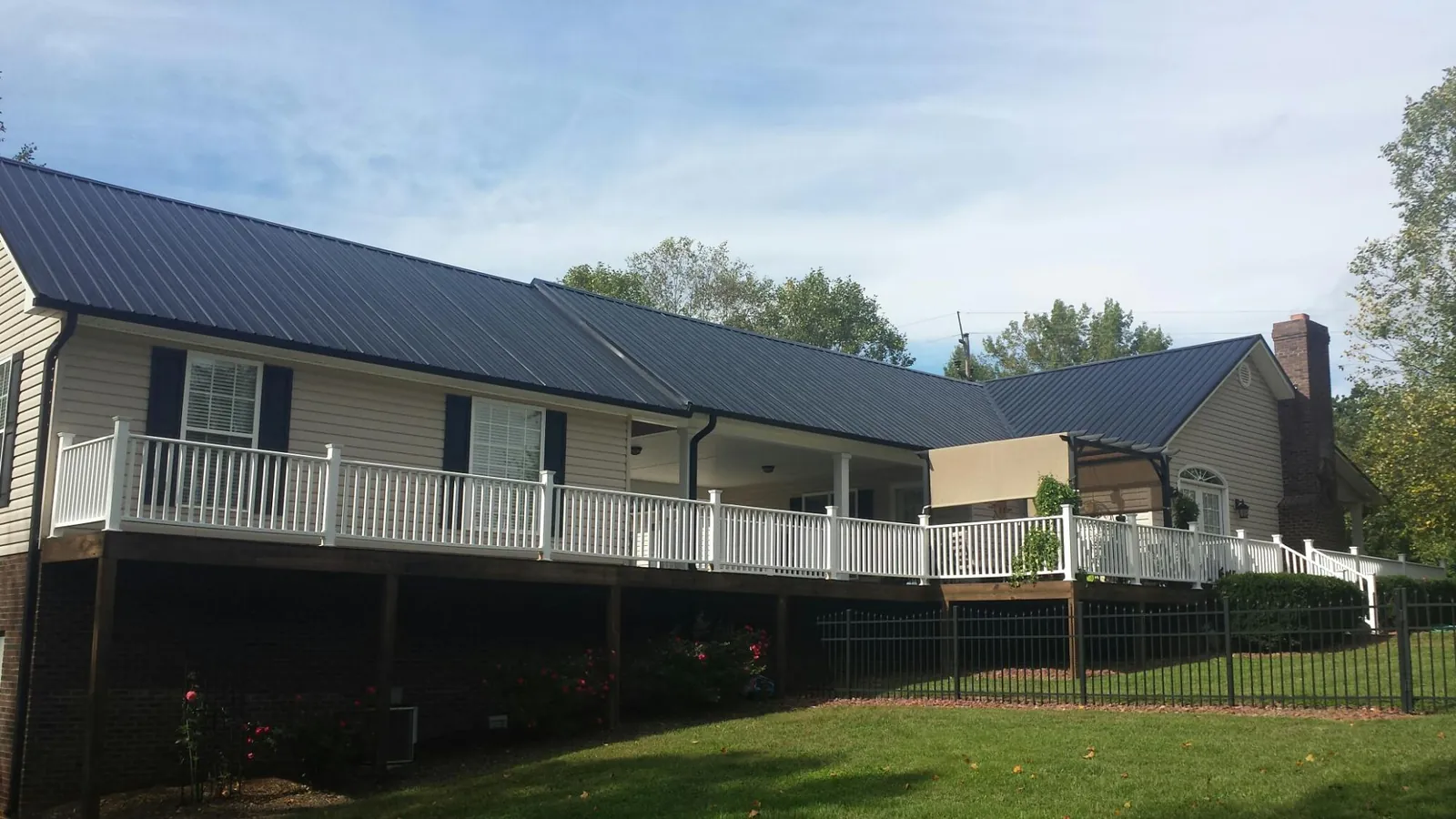 Black metal roof above a long white railed deck on a hillside home in Kennesaw