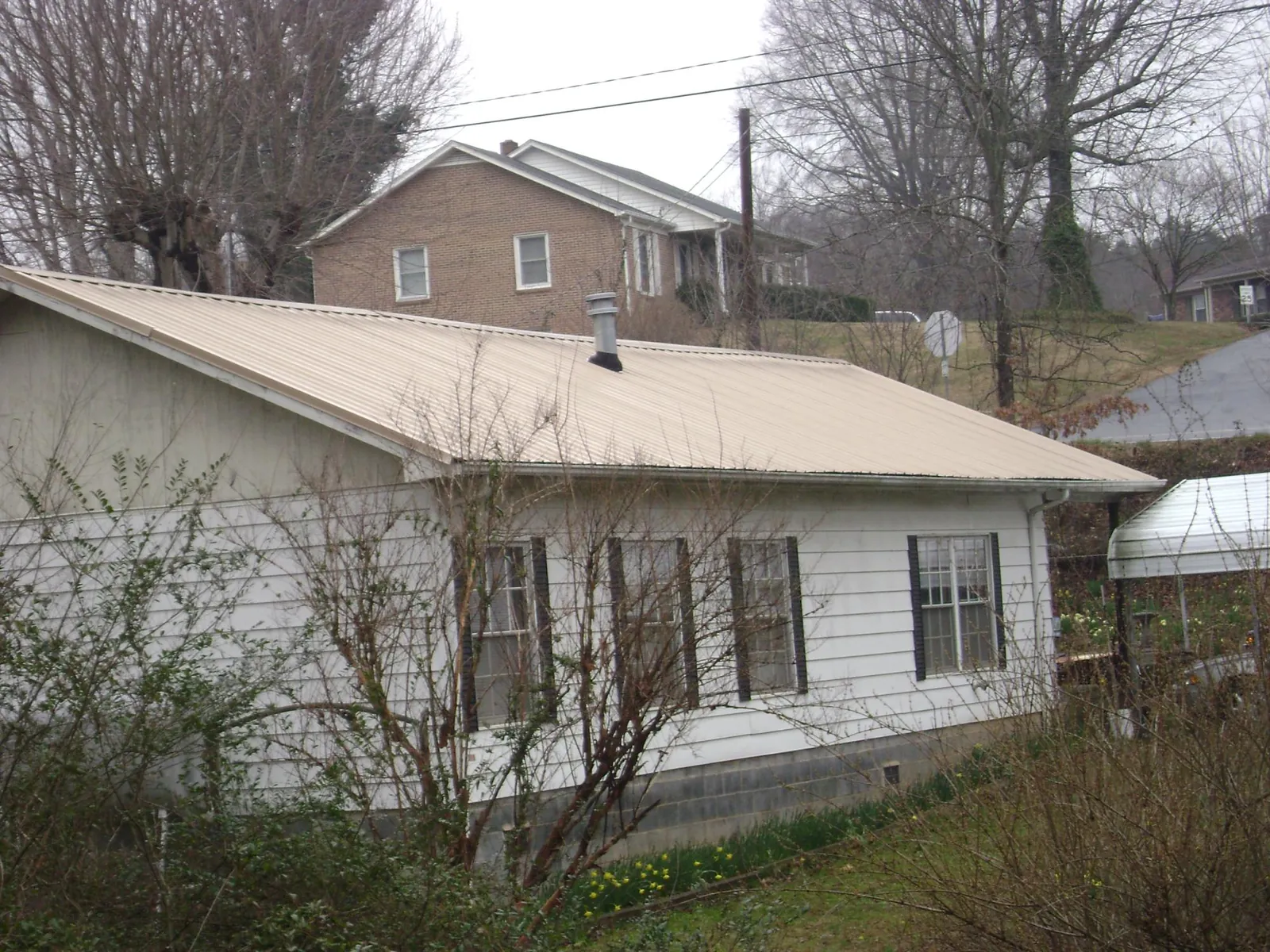 Tan metal roof on a white sided house set into a hillside — Commercial Roofing by Roofing Brothers in Kennesaw